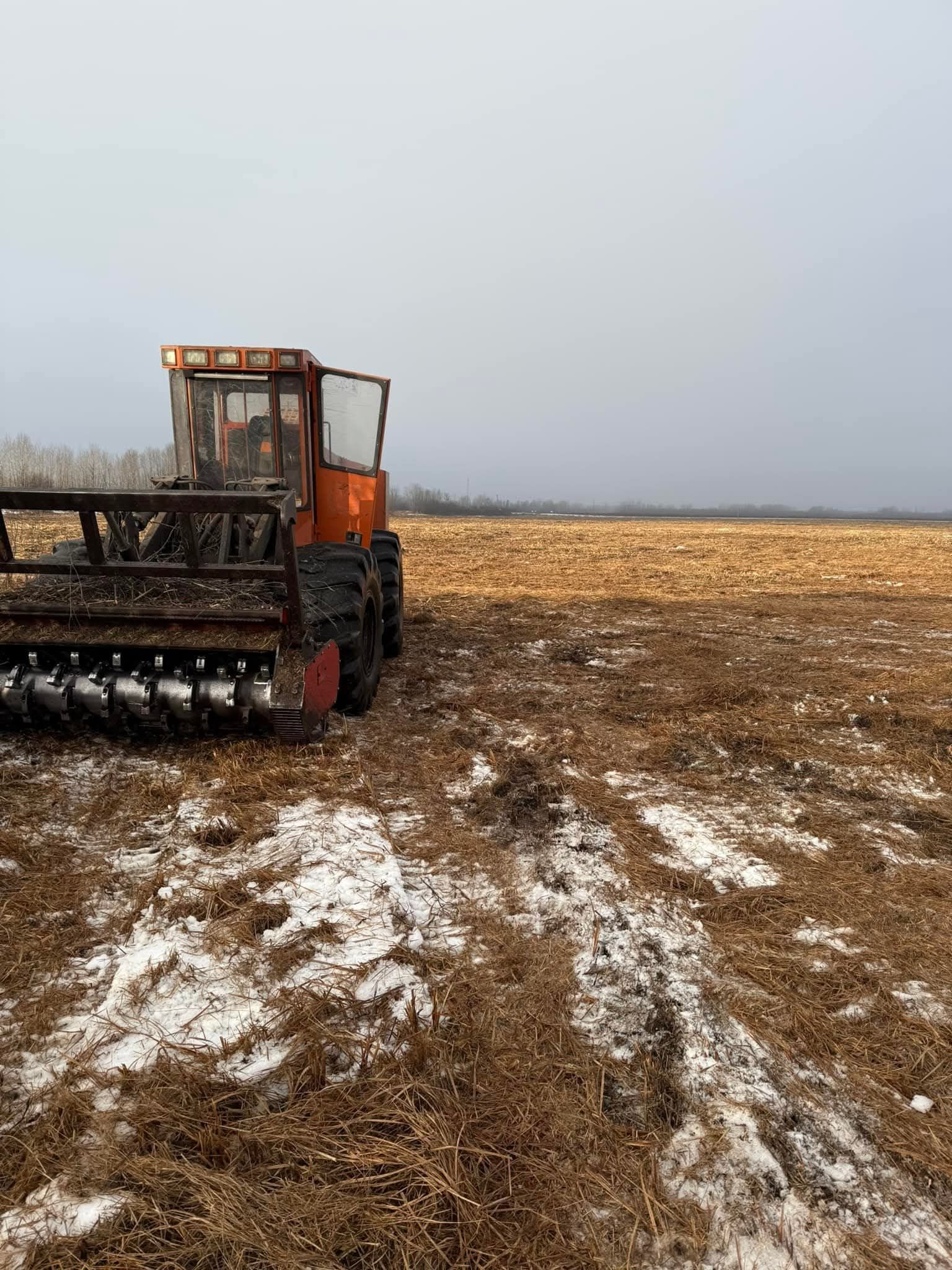 A tractor is plowing a field with snow on the ground.
