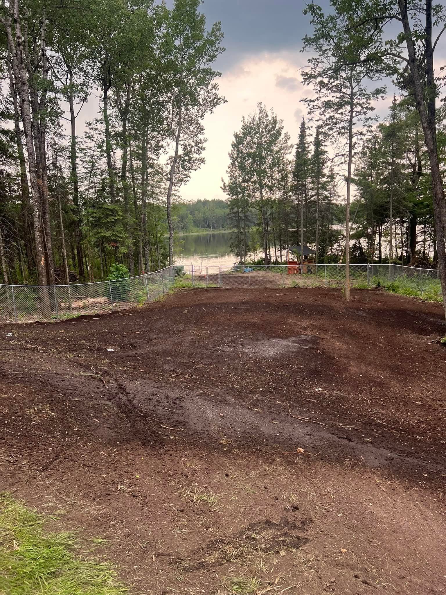 A dirt road leading to a lake surrounded by trees on a cloudy day.