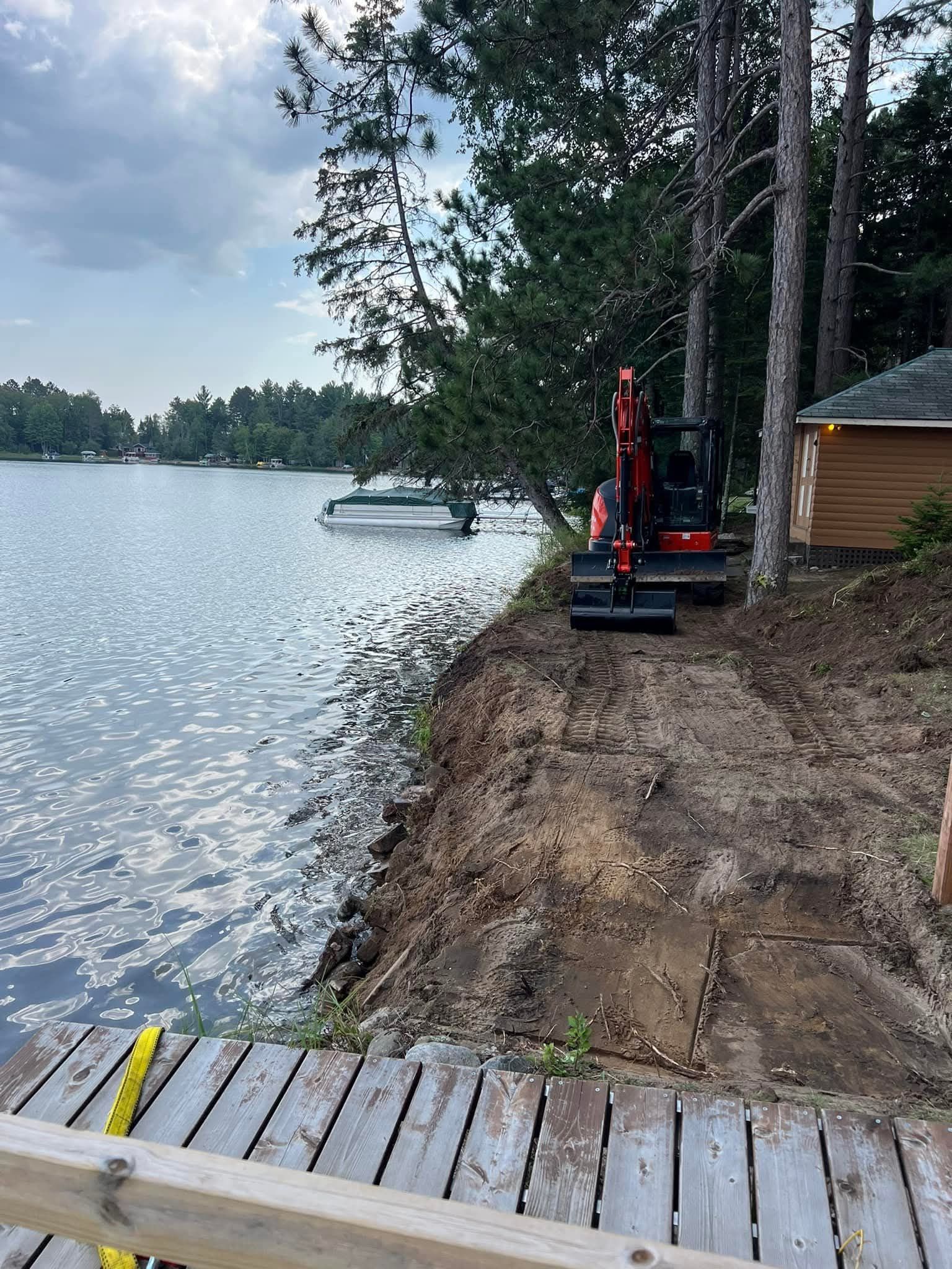 A small excavator is working on a dirt road next to a lake.