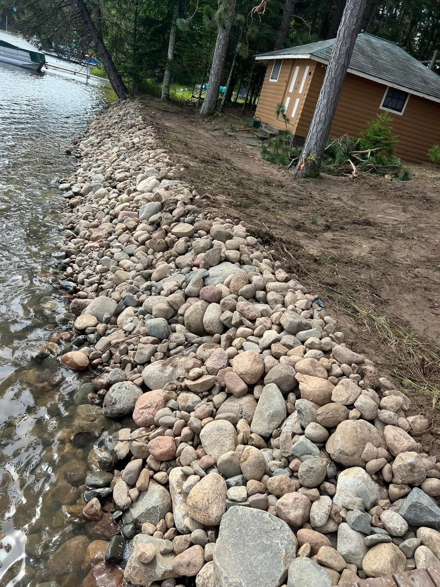 A pile of rocks on the shore of a lake next to a house.
