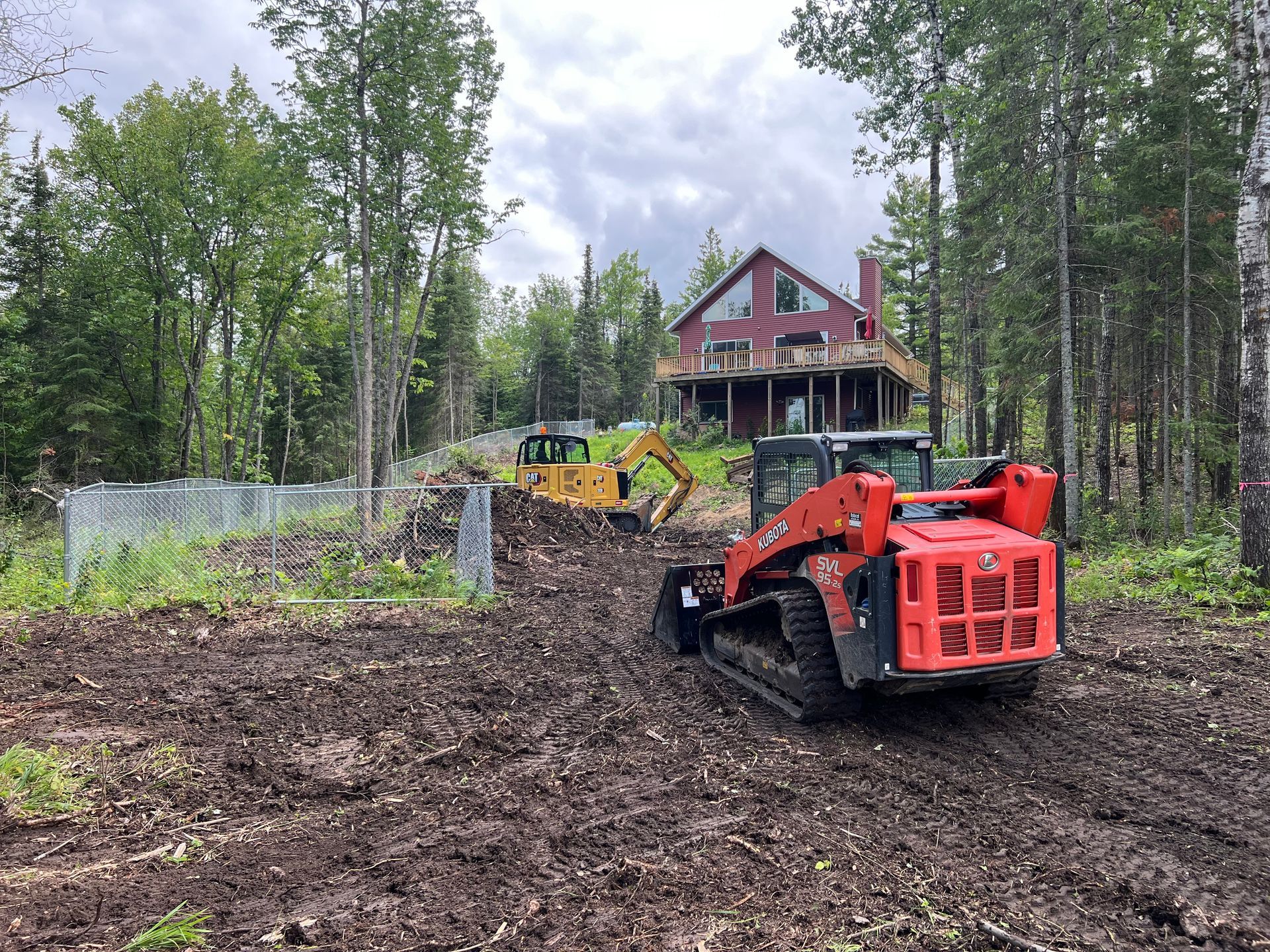 A red bulldozer is driving through a dirt field in front of a house.