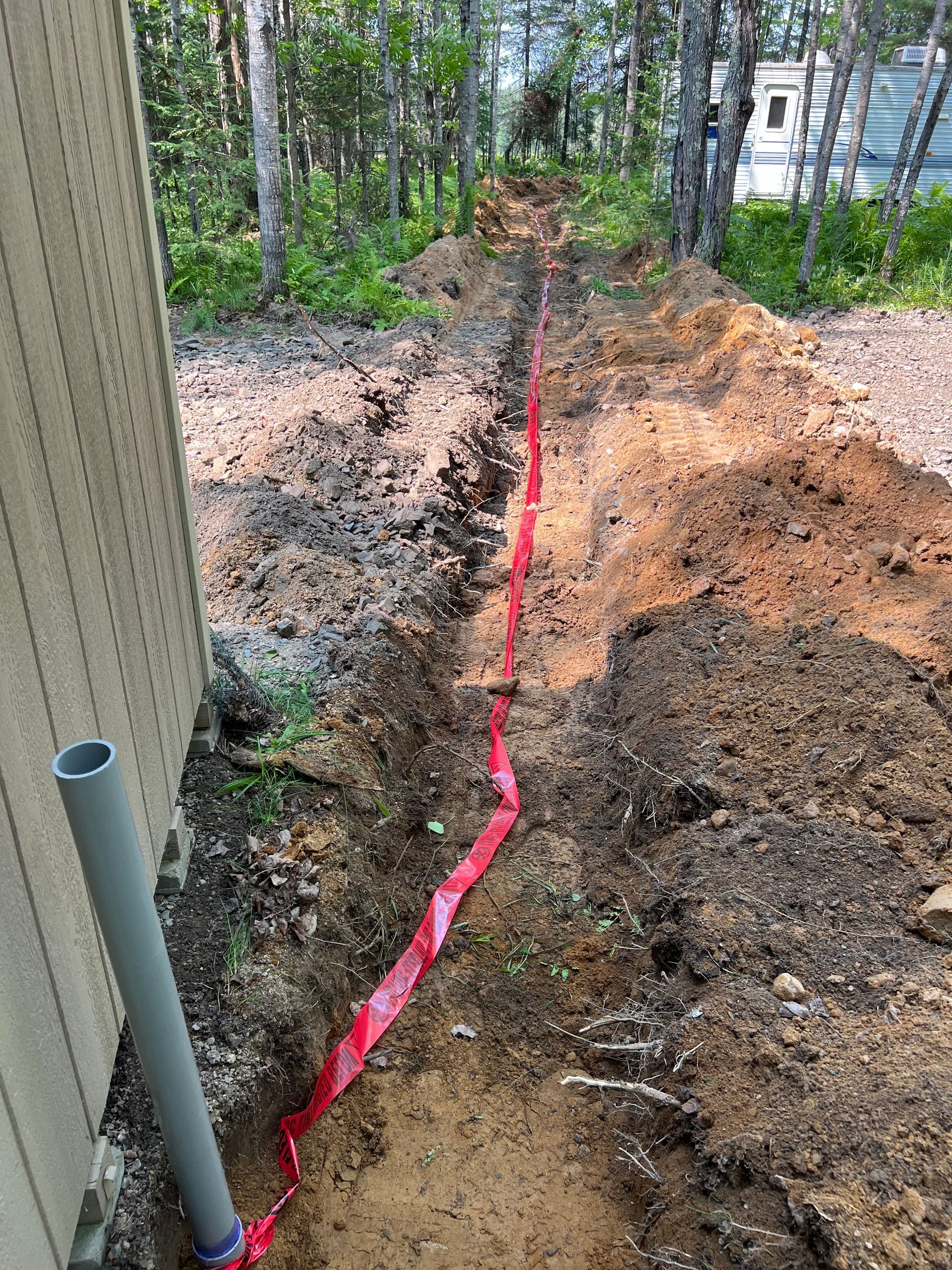 A pipe is being installed in the dirt next to a house.