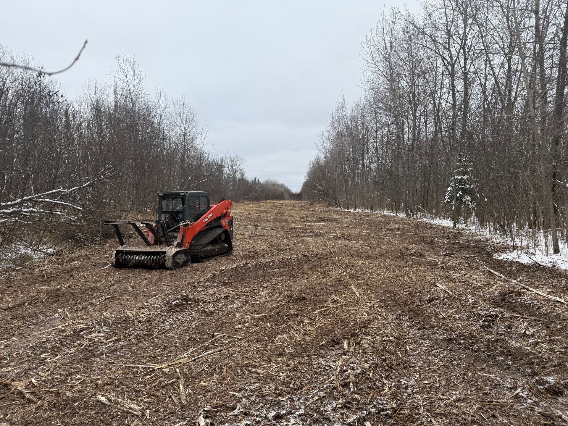A tractor is driving down a dirt road in the woods.