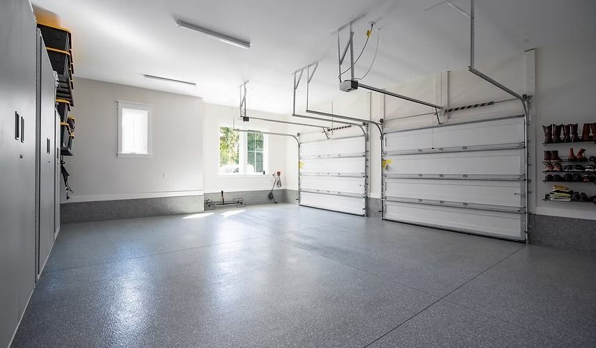 Empty, clean garage with gray floor, white walls, two open garage doors, and storage cabinets.