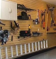 Garage interior with slatted walls, tools, storage shelves, and a ladder.