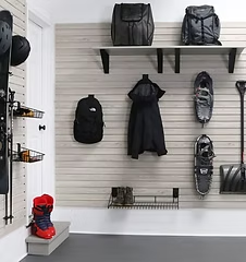 Garage storage system with shelves and hooks holding bags, shoes, coats, and a snow shovel.