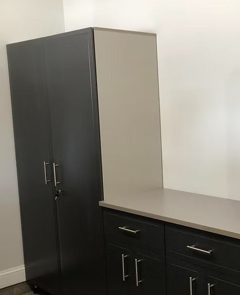 Gray storage cabinet and black cabinets with drawers and countertop against a white wall.