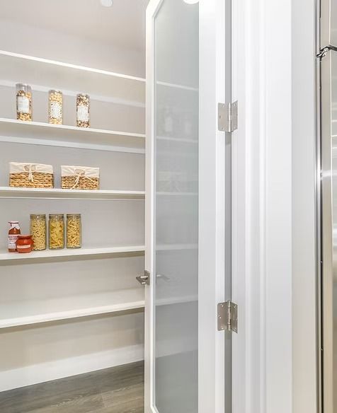 White pantry with open glass door, shelves stocked with food items.