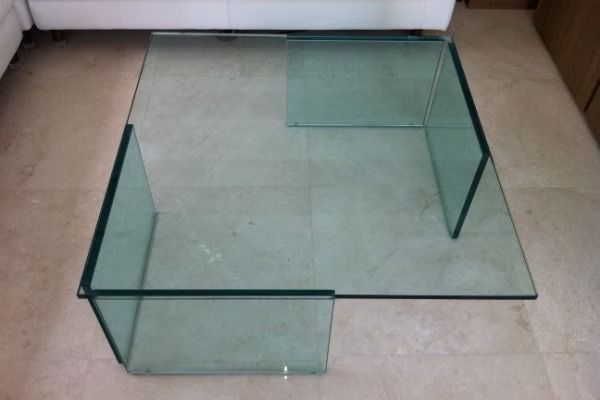 Glass coffee table with angled legs on a tiled floor.