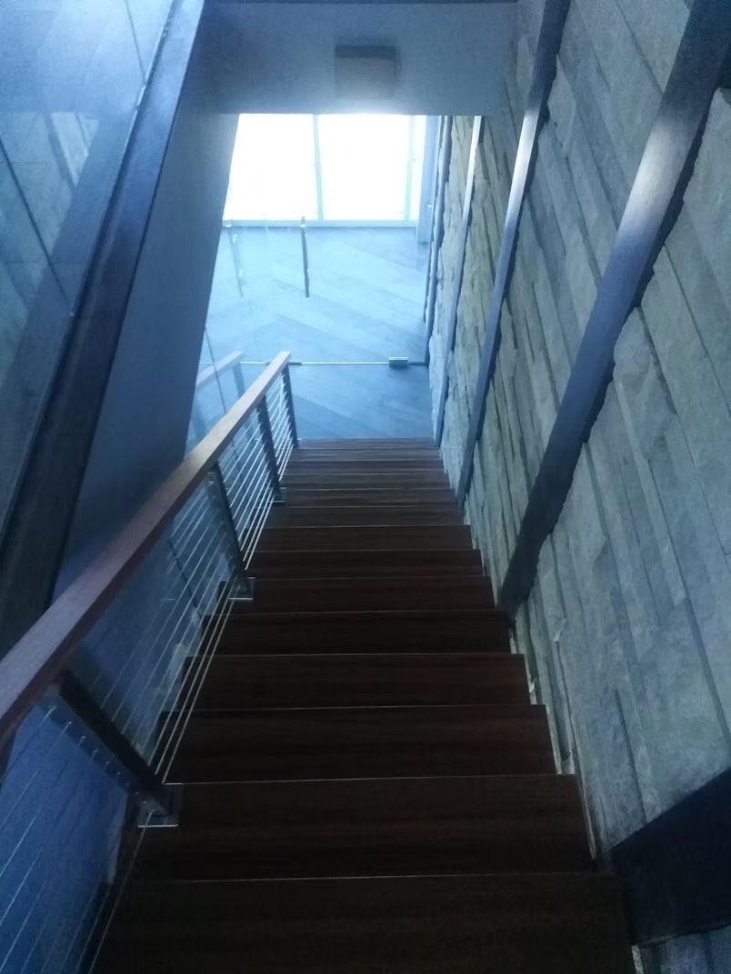 Staircase ascending towards a skylight. Wooden steps with metal and wood railings between blue-gray walls.