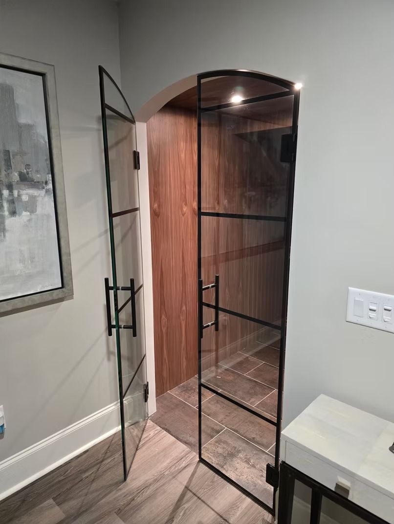 Glass door with black gridwork, leading to a small room with wood walls and tiled floor.
