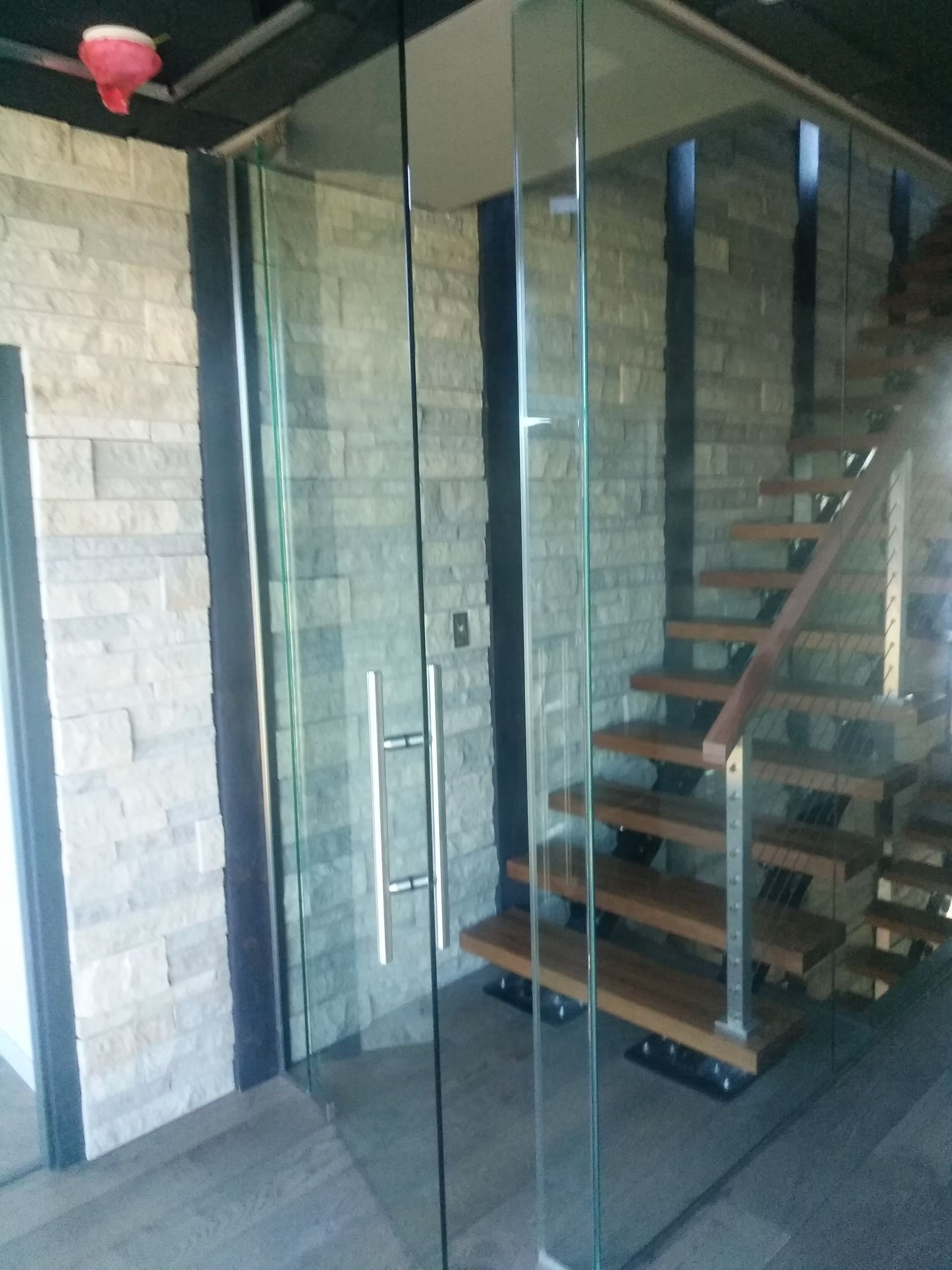 Glass-walled interior with stone wall and wooden staircase.