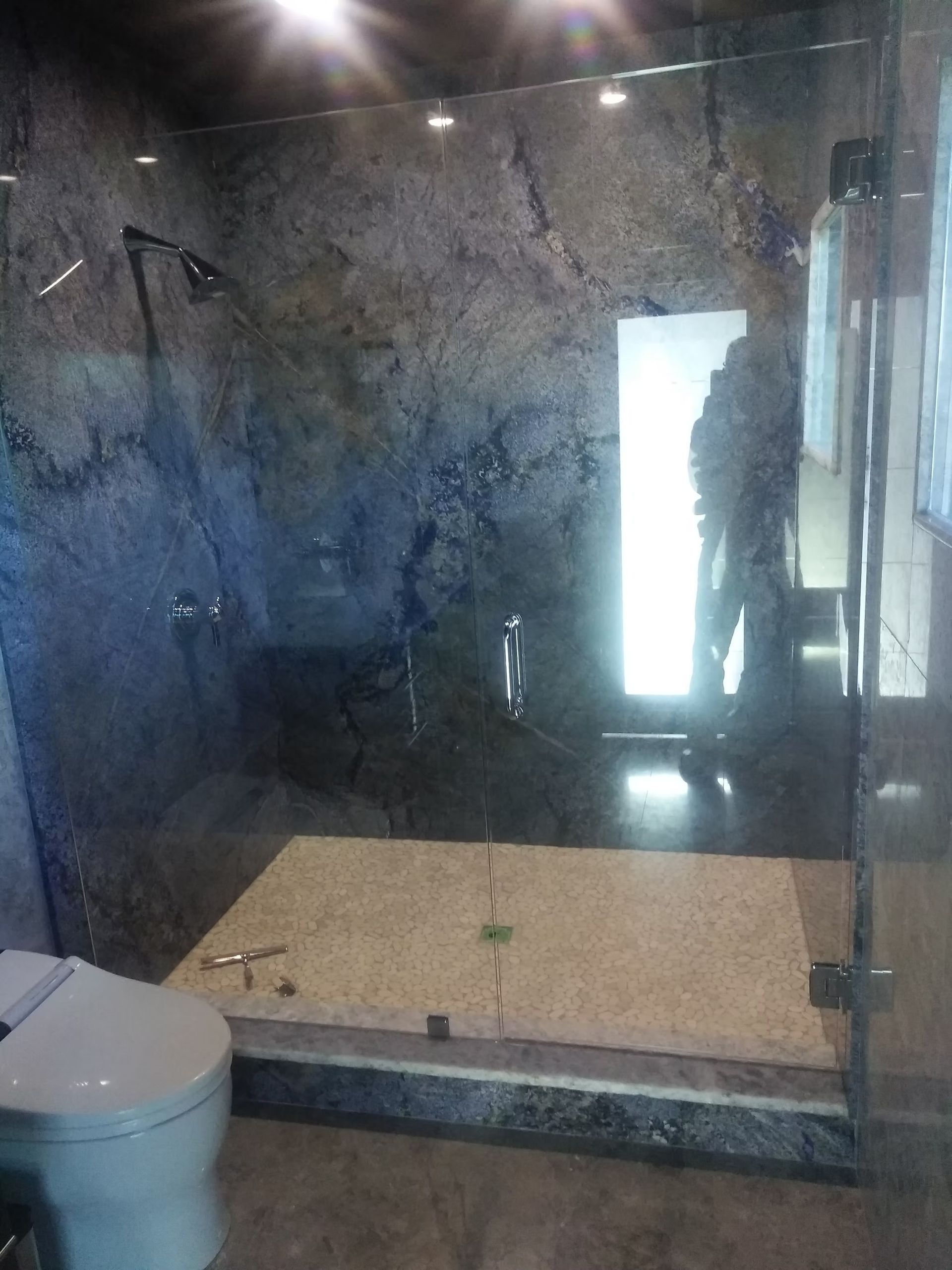 Shower with granite walls, glass door, and a light-filled opening. Toilet on left.