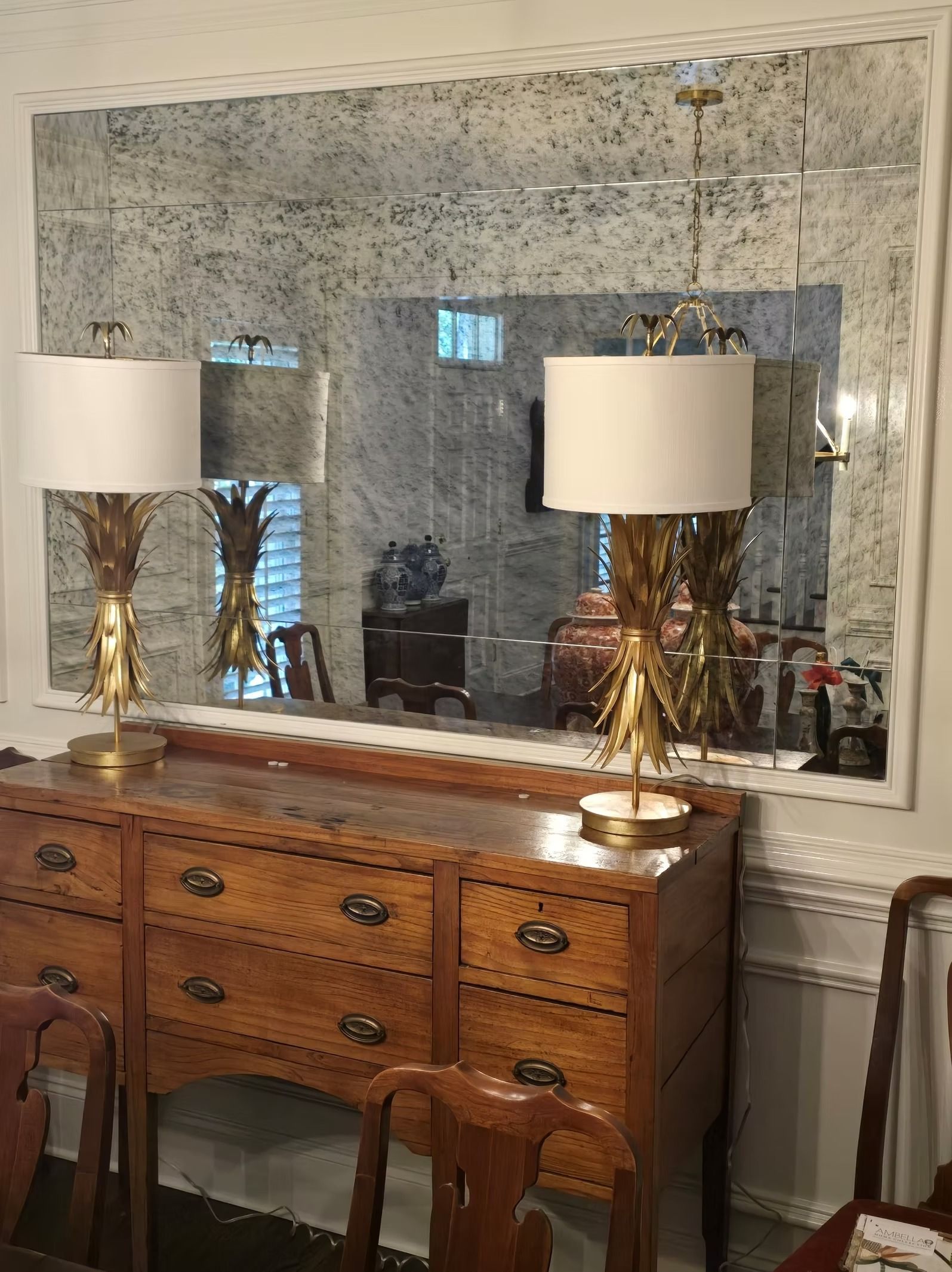 Antique buffet with lamps beneath a large distressed mirror.  A window is reflected in the mirror.