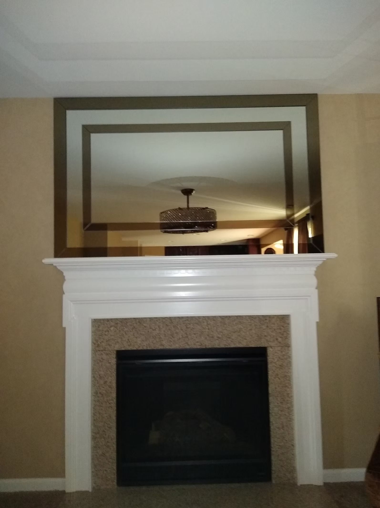 Fireplace with white mantel, a granite-like facade, and a large rectangular mirror reflecting a ceiling fan.