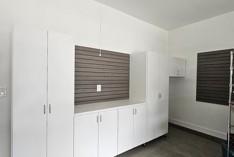 White garage cabinets and shelving, with a dark gray pegboard and a small window.