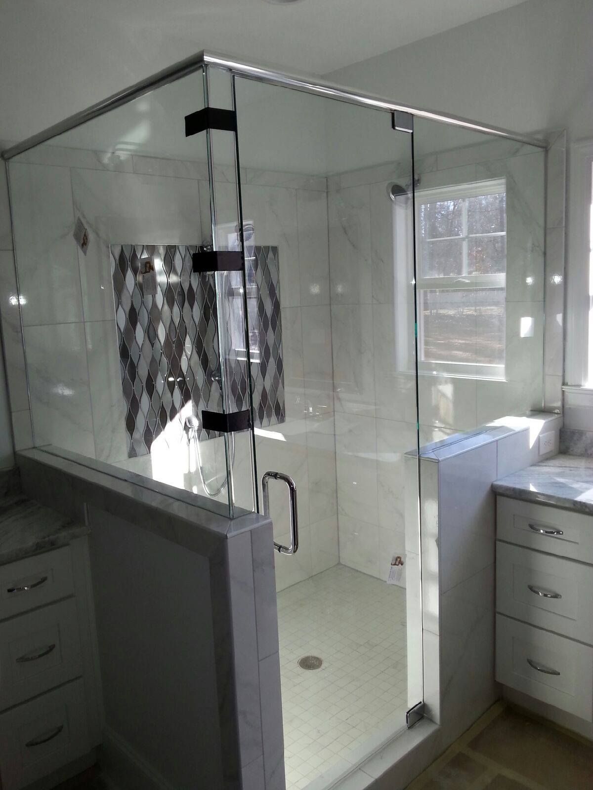 Glass shower enclosure in a bathroom with white tile and cabinetry.