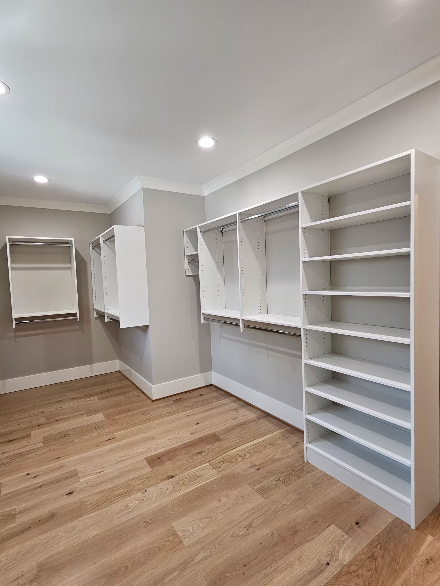 Empty walk-in closet with white shelves, hanging rods, and light-colored hardwood floors.