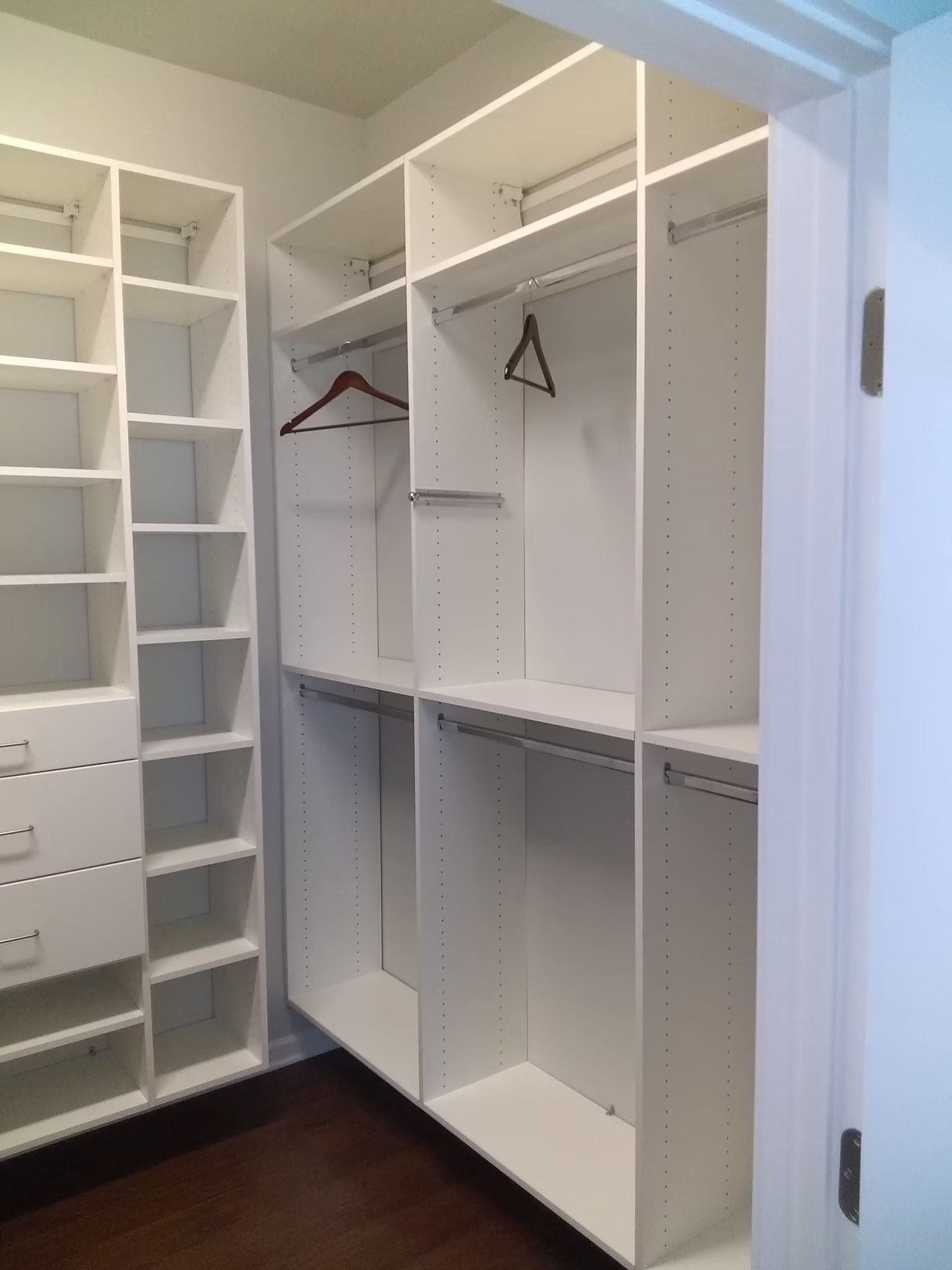 White built-in closet with shelves, drawers, and hanging rods. Closet is empty, viewed from doorway.