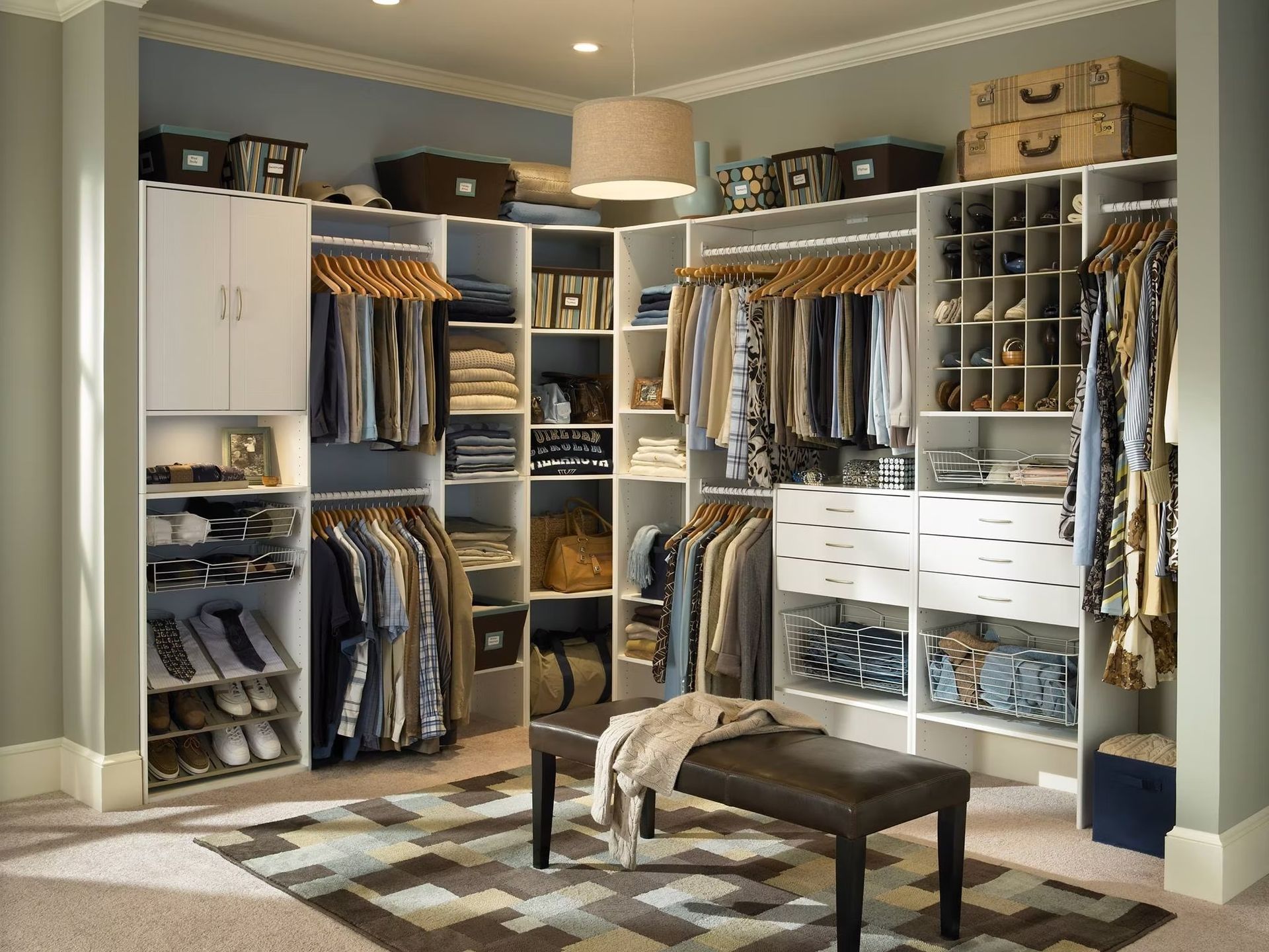 Walk-in closet with white shelving, hanging clothes, drawers, shoe racks, and a bench on a patterned rug.