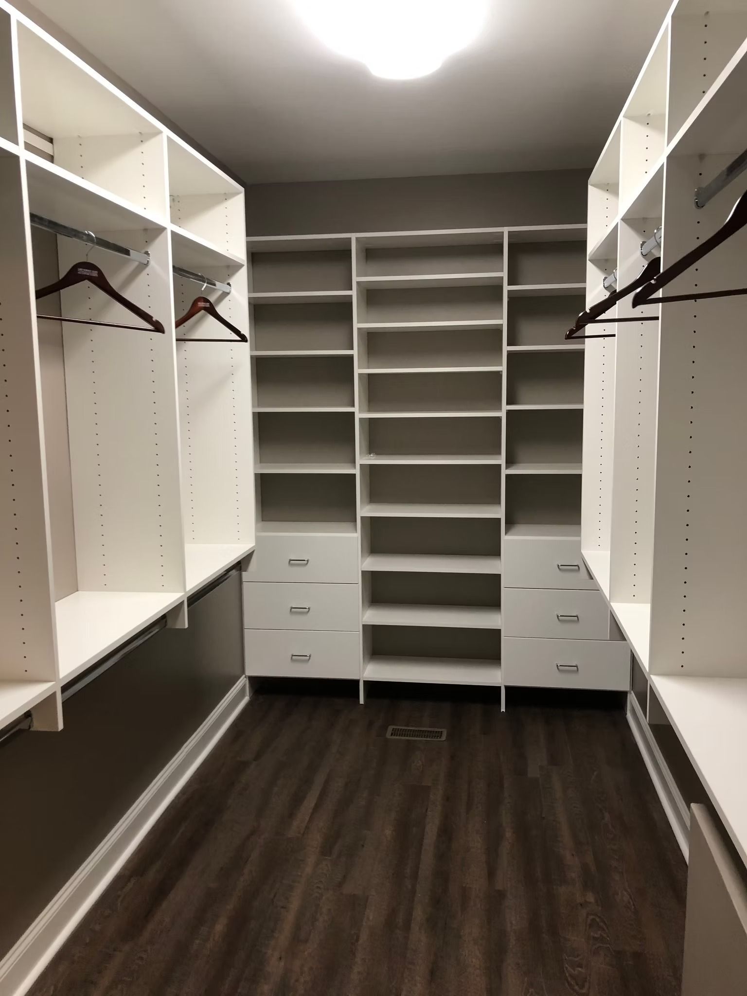 Walk-in closet with white shelving, dark wood floor, and hanging clothes.