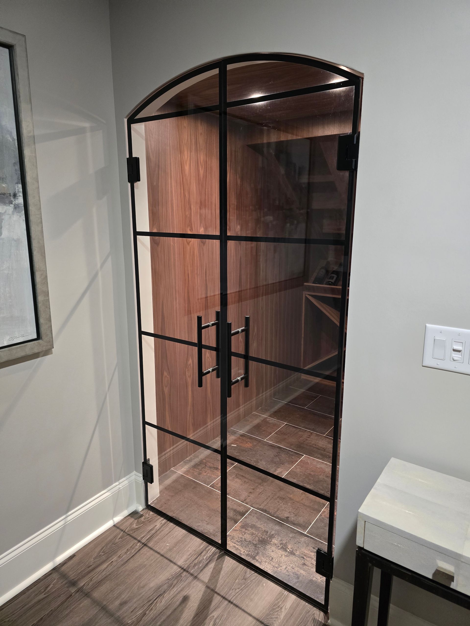 Glass wine cellar door with black metal frame and handle.