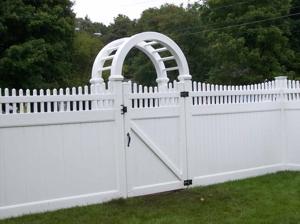 White vinyl picket fence with a central gate and arched trellis over a grassy yard.