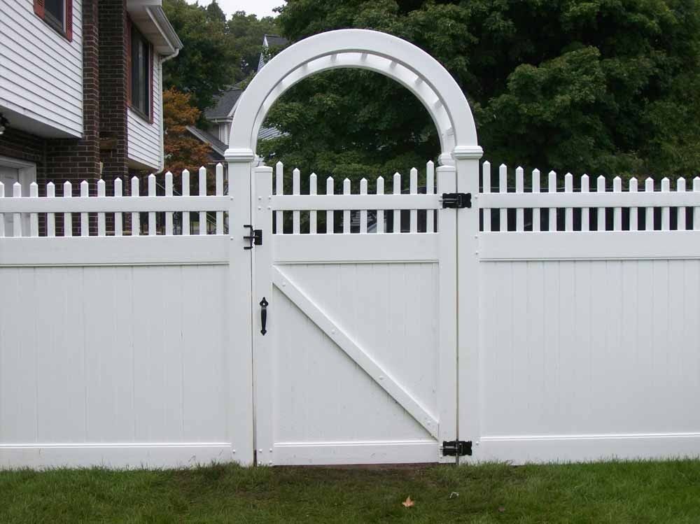 White picket fence with a small arched garden gate in front of a house and trees