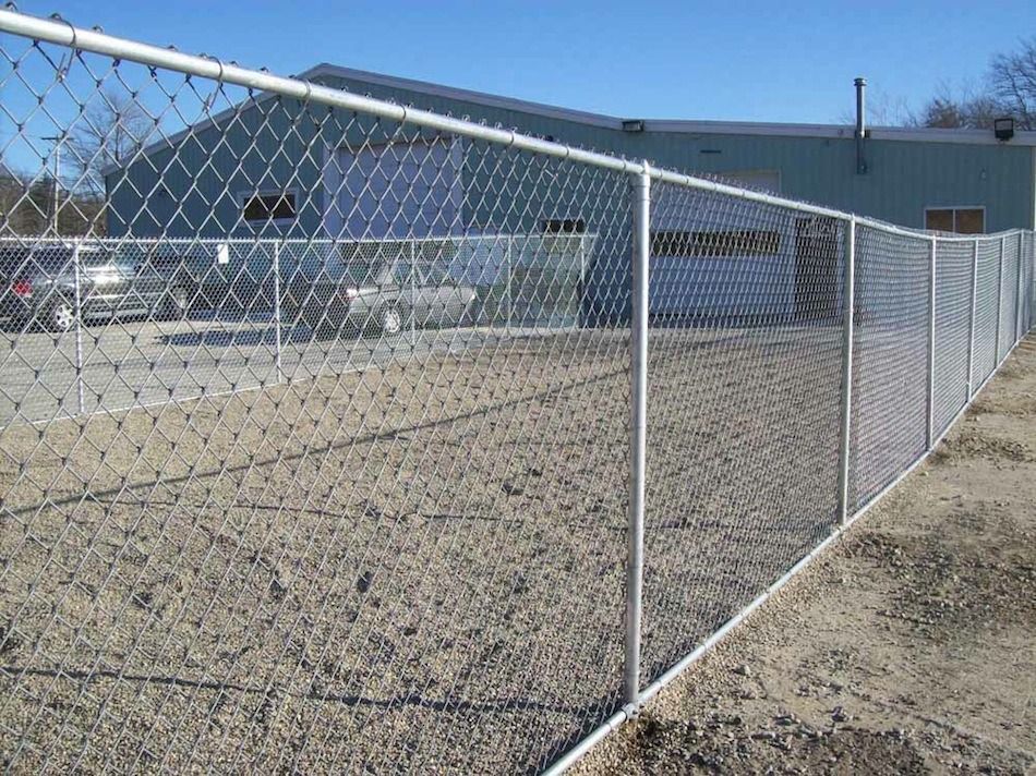 Chain-link fence enclosing a gravel lot beside a blue industrial building under a clear sky