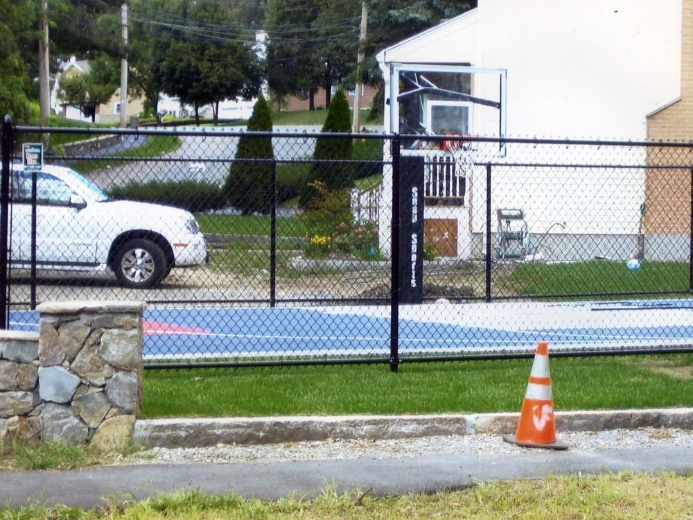 Orange traffic cone on a sidewalk beside a chain-link fence and parked car near a building
