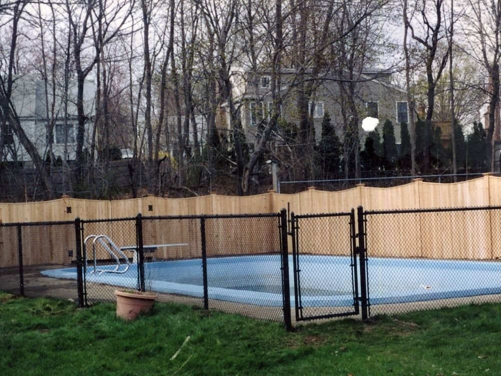Outdoor tennis court with blue surface, black fence, and leafless trees behind it.