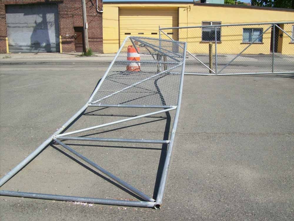 Collapsed metal fence barrier lying across an asphalt lot near a yellow building