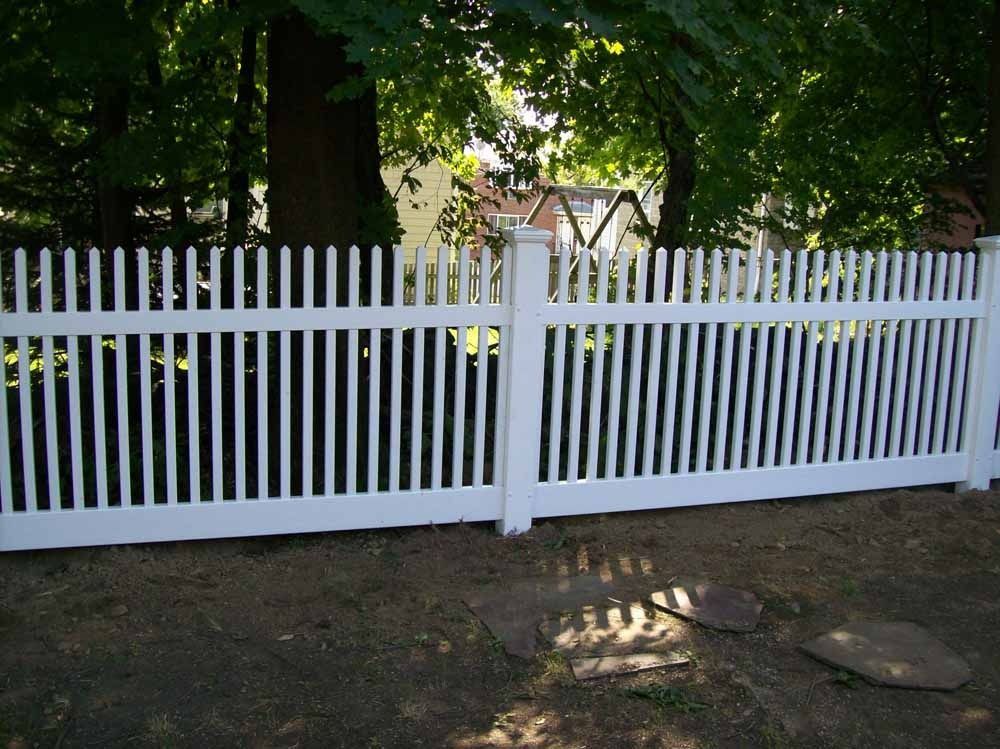 White picket fence with a gate in a shaded yard, with trees and sunlight behind it