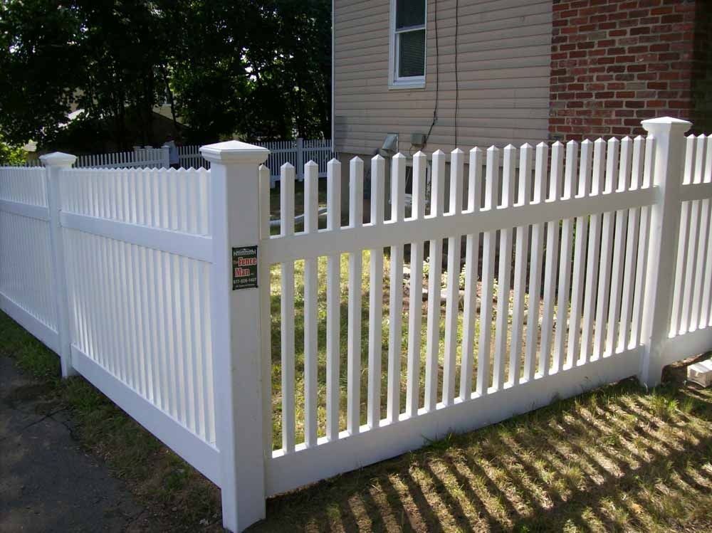 White picket fence with gate beside a house in a sunny yard