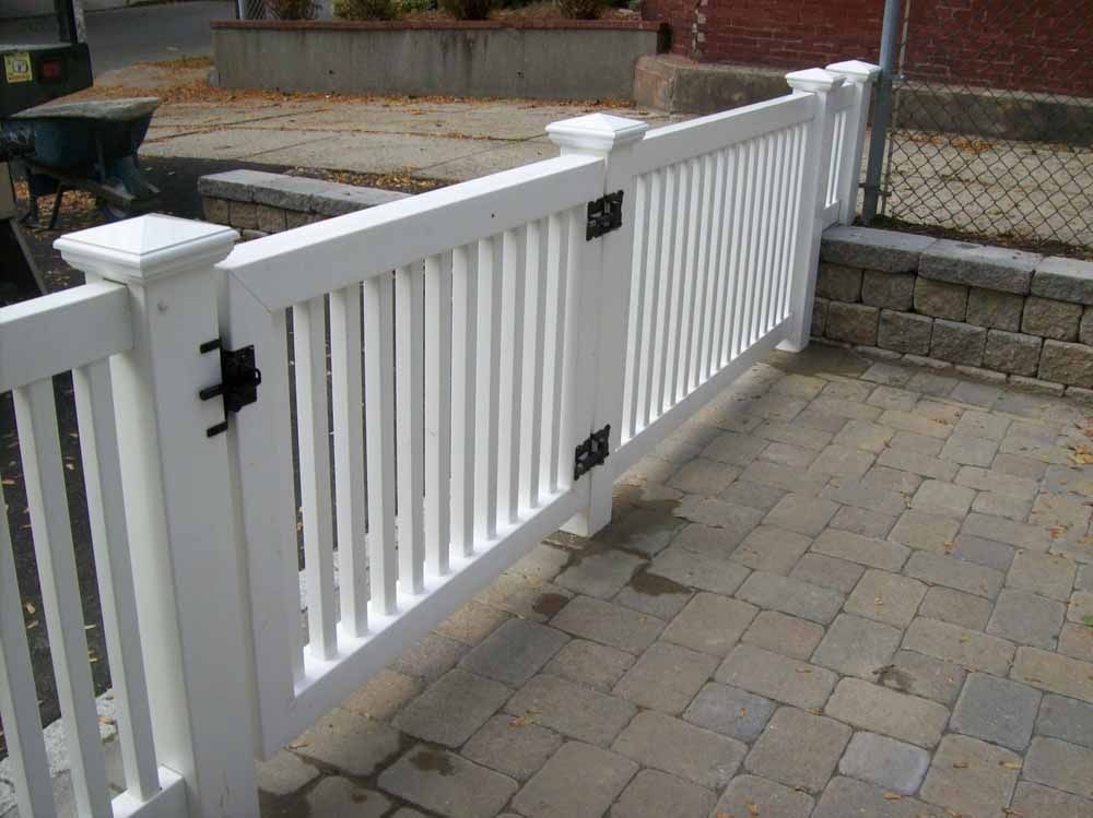 White metal gate between brick walls beside a paved walkway and steps