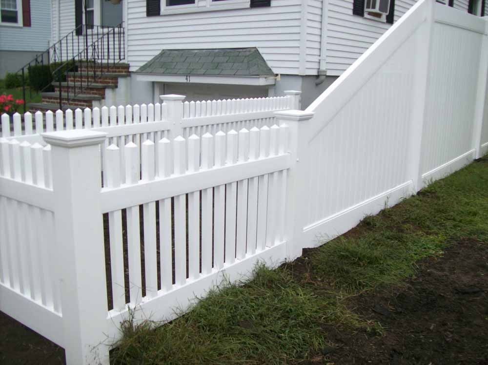 White vinyl fence and gate along a grassy yard beside a house