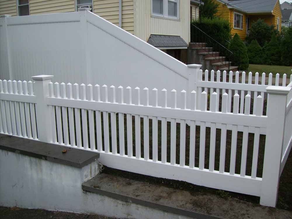 White picket fence with a sloped gate beside a house and driveway