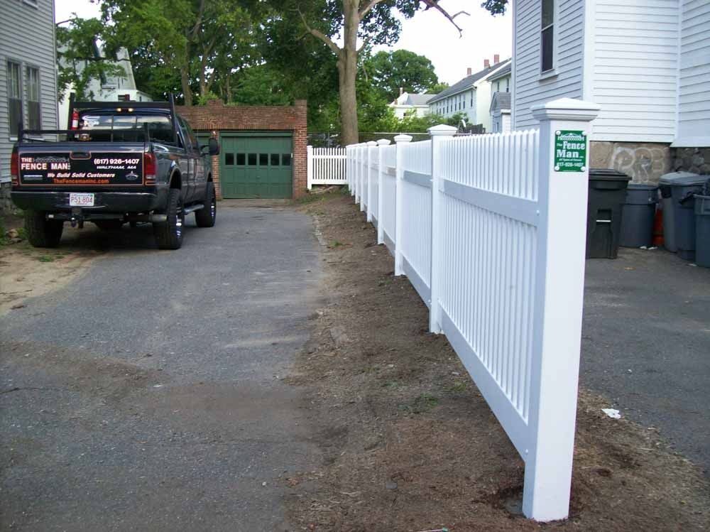 White picket fence lining a driveway beside a house, with a black pickup truck parked near a garage.