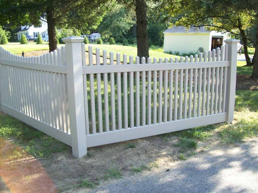 White wooden picket fence enclosing a yard with trees and a house in the background