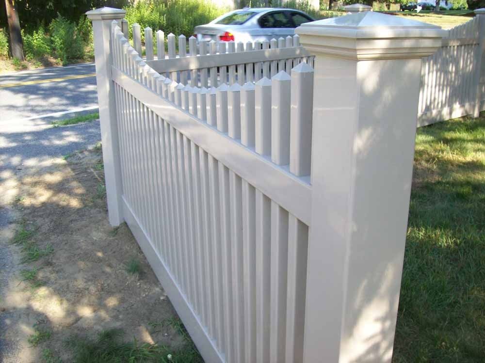 White picket fence and gate along a suburban driveway, with a car parked behind it.