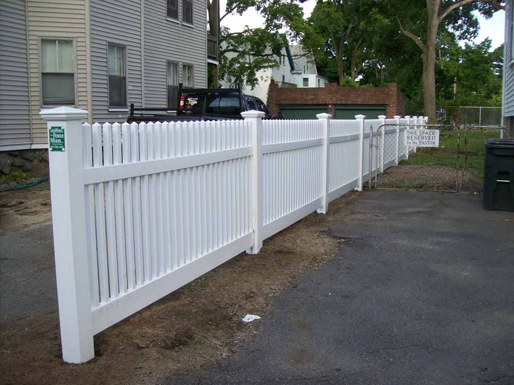 White picket fence lining a paved driveway beside a house and parked car