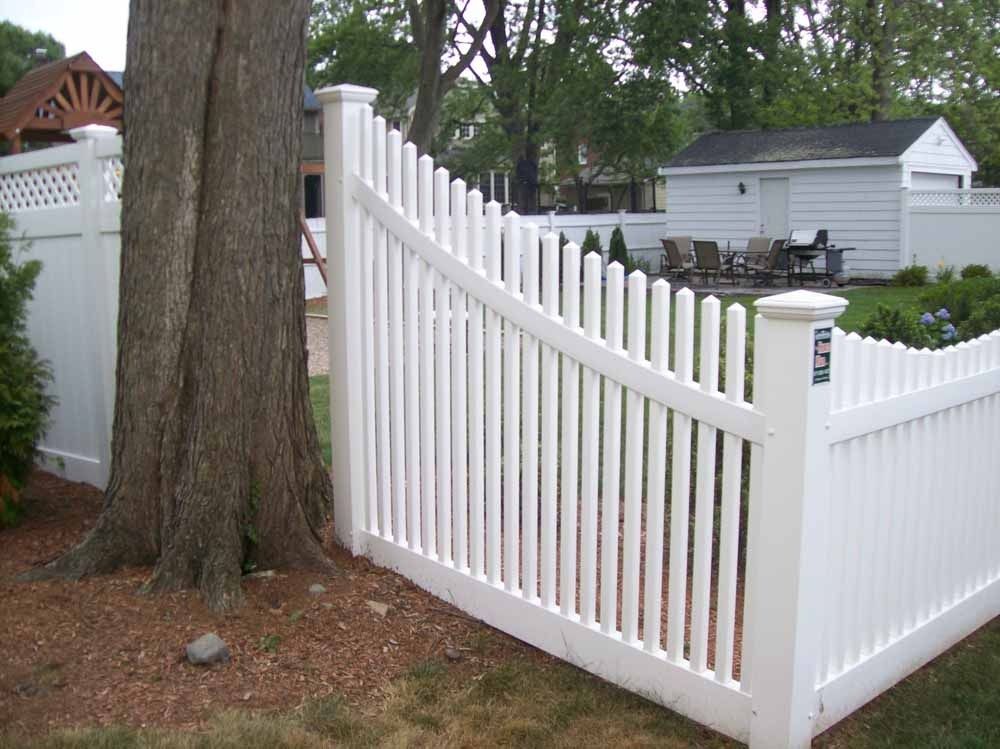 White picket fence curving around a yard beside a large tree and driveway.