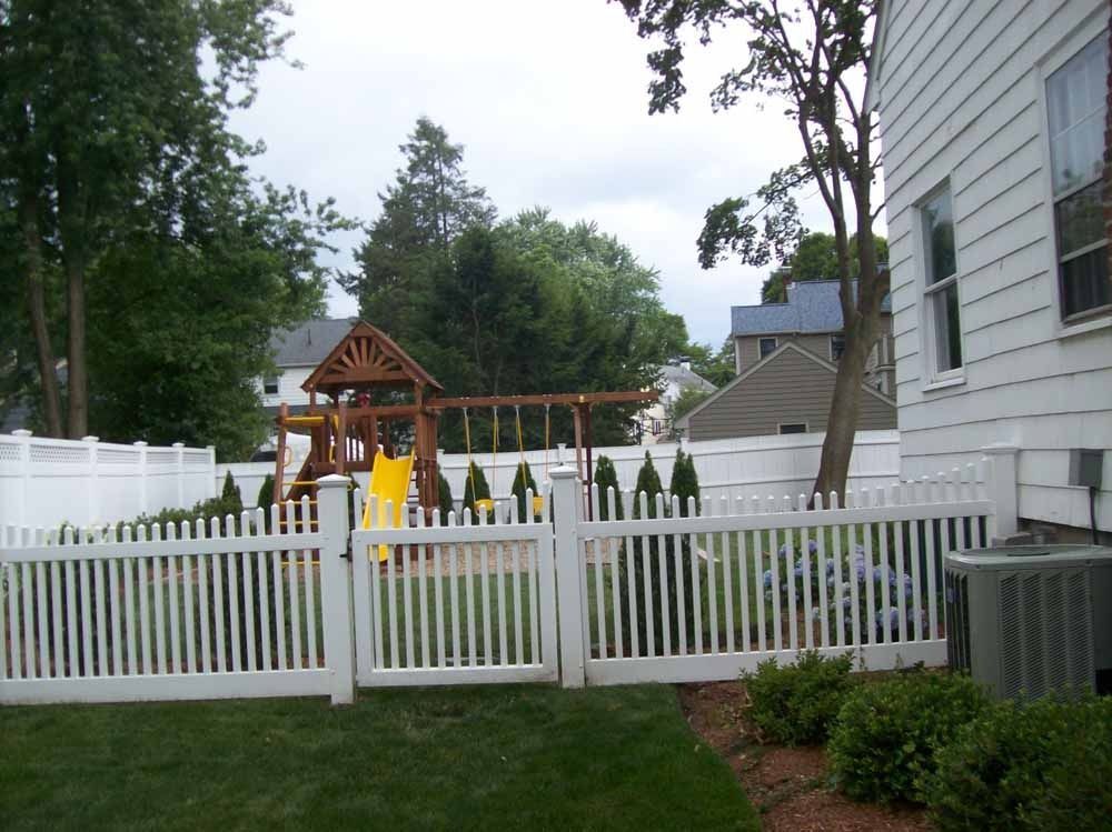 Backyard playset behind a white picket fence beside a house