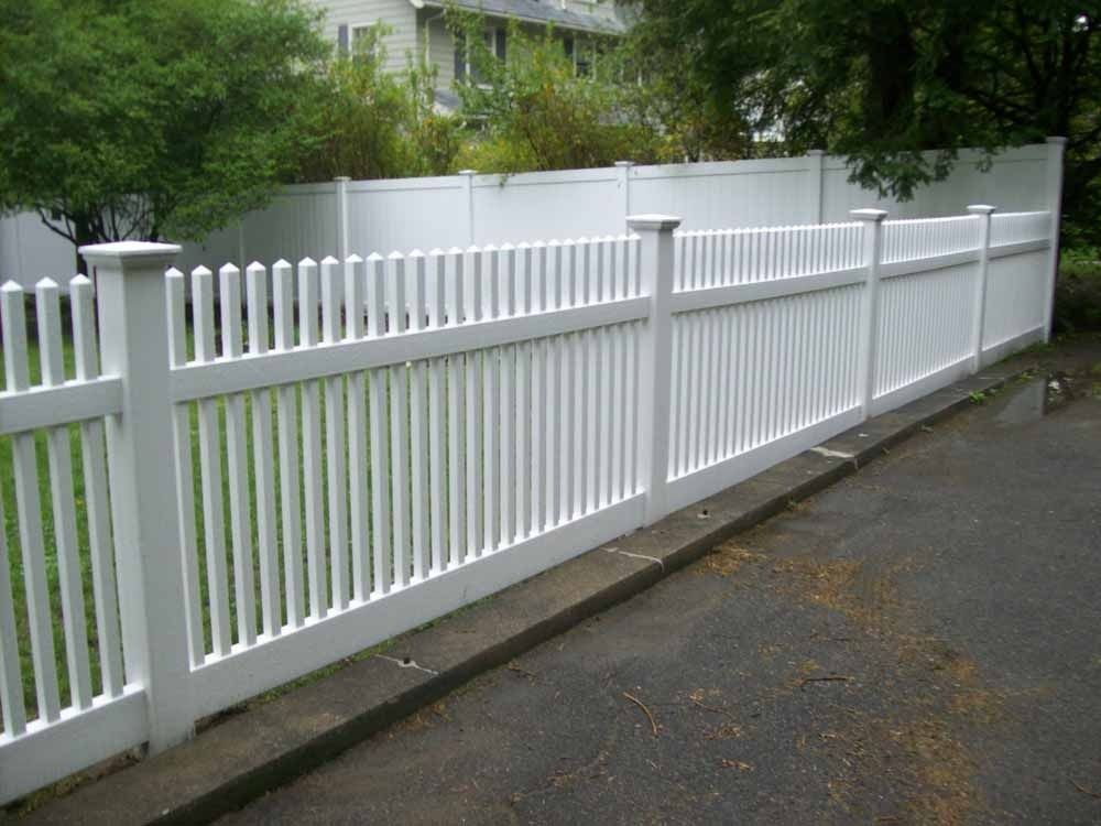 White picket fence along a wet roadside beside a grassy yard and trees