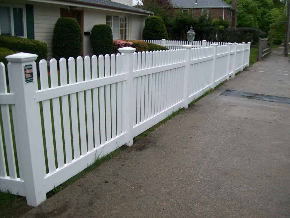 White picket fence along a residential sidewalk beside a house and hedge-lined street