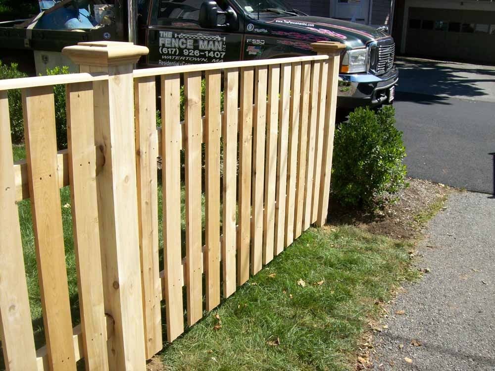 Wooden fence along a sidewalk beside a parked car and bushes
