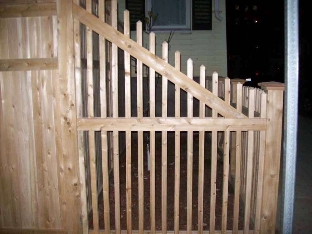 Wooden backyard gate with diagonal cross-bracing and vertical slats at night