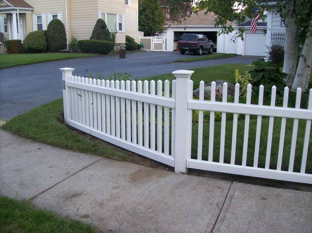 White vinyl picket fence along a suburban sidewalk and driveway in front of a house