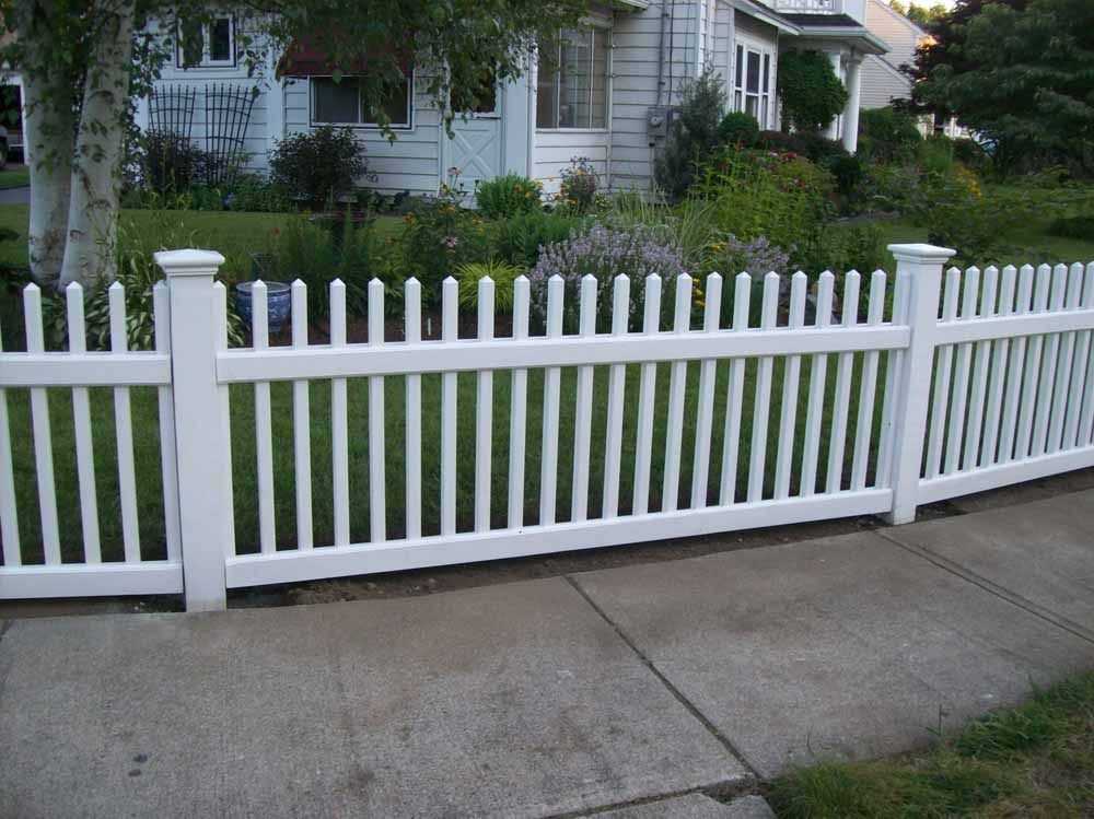 White picket fence along a suburban sidewalk in front of a house and lawn.