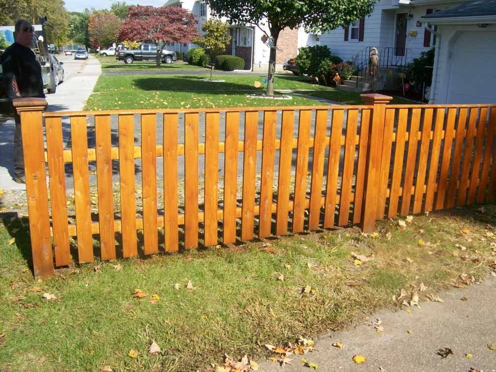 Orange wooden fence along a sidewalk in a residential yard with green grass and autumn leaves.